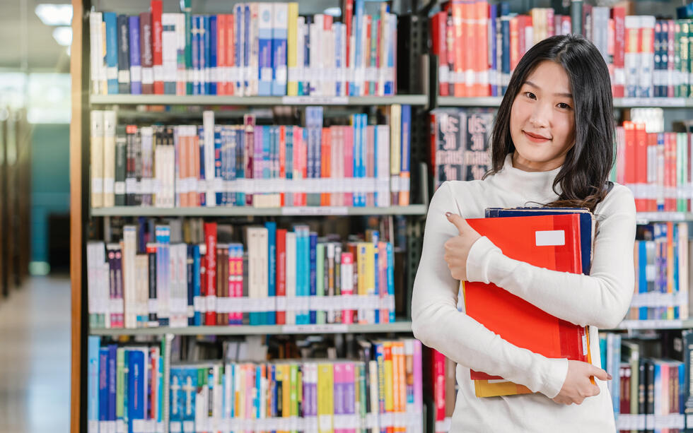 Student standing in front of bookcase, deciding on books to use for study. Take an experienced teacher's recommendation for the best book to use for learning Mandarin Chinese.