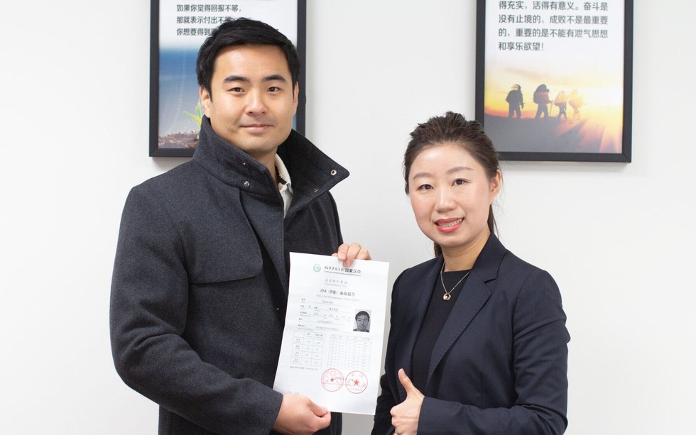 Student experiences success with an experienced Mandarin Chinese teacher. Student of Chinese for Professionals poses with teacher, holding award with excellent HSK test results while teacher gives thumbs-up.